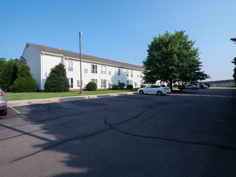 A white car is parked in front of a white building with a brown roof.