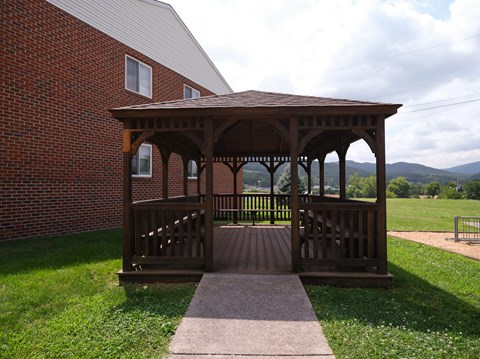 A wooden gazebo with a brick building in the background.
