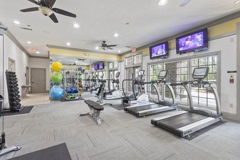 a gym with treadmills and other exercise equipment and two televisions on the wall