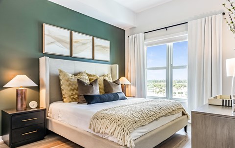 A bedroom with a large bed, a nightstand with a lamp, and a window with curtains.