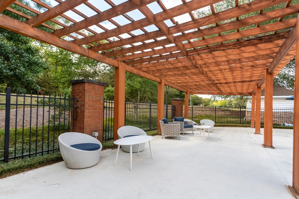 A patio with a white table and chairs under a wooden pergola.