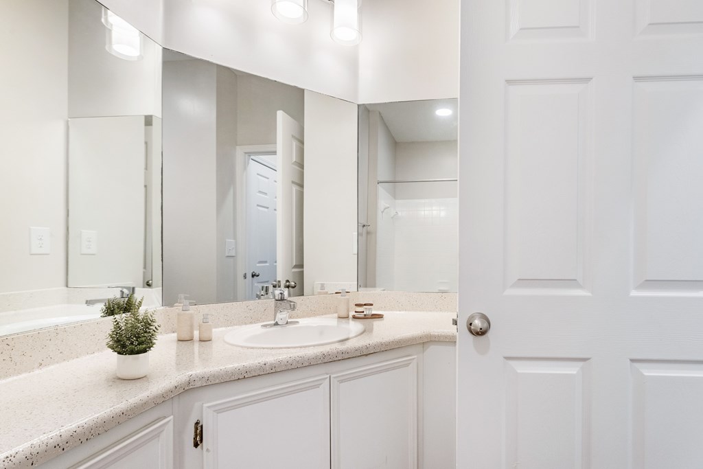 A white bathroom with a sink, mirror, and a plant.