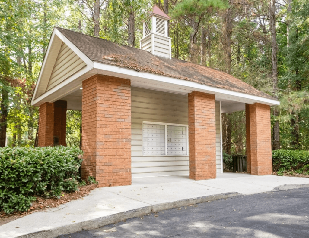 A small building with a steeple and a white door is surrounded by greenery.