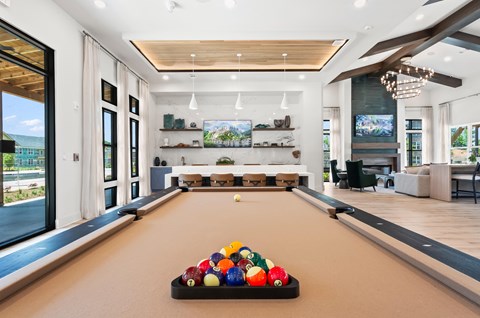 A pool table with a variety of balls on it in a room with a lot of windows.