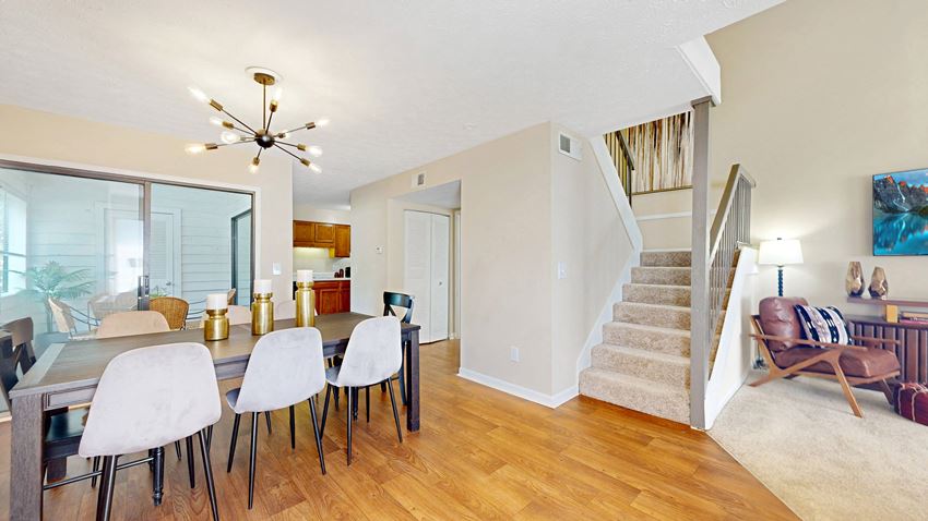 a dining area with a table and chairs and a staircase in the background - Photo Gallery