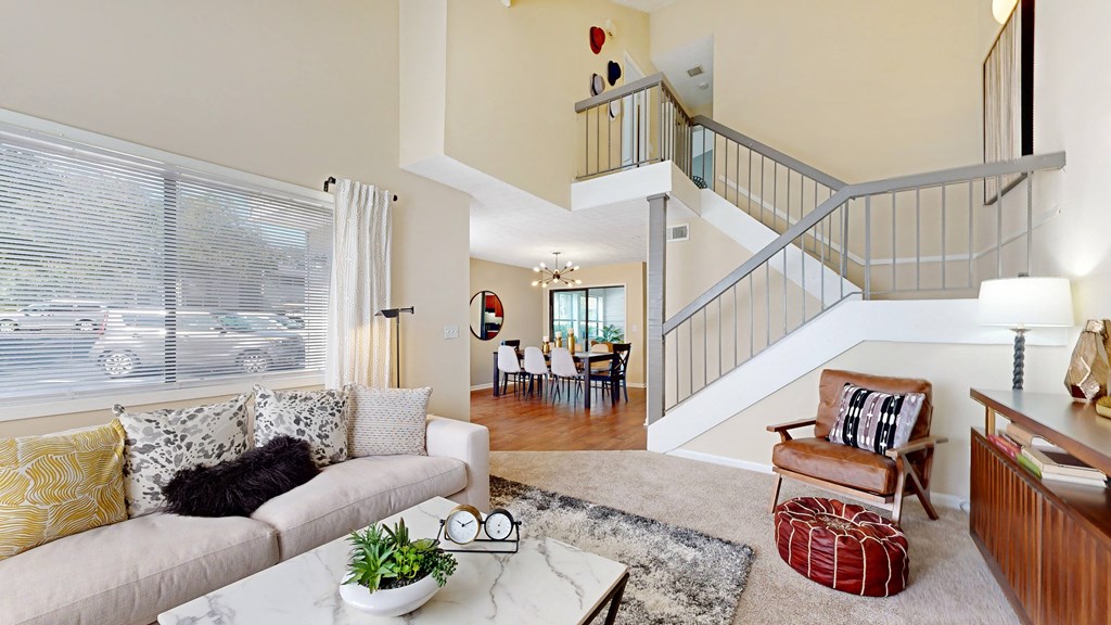 a living room with a staircase in the background and a couch and chair in the foreground