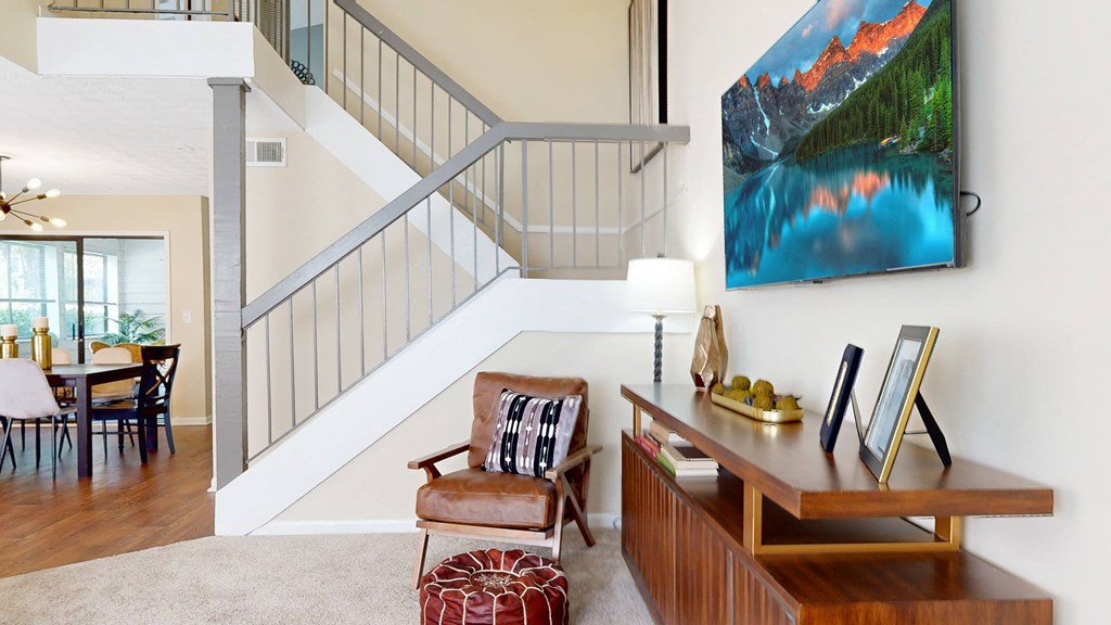 a living room with a staircase in the background and a desk and chair in the foreground