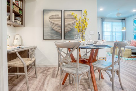 A dining room with a table set for two and a vase of yellow flowers.