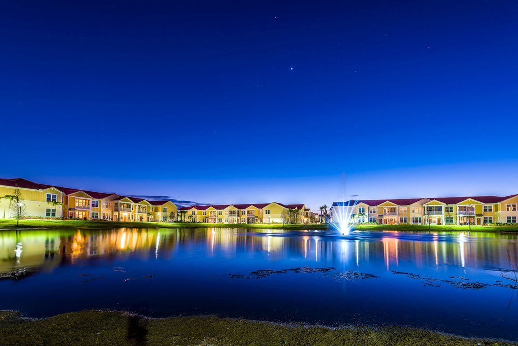 a fountain in the middle of a lake with houses in the background