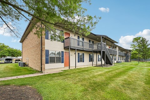 A building with a balcony and a red door is surrounded by a green lawn.