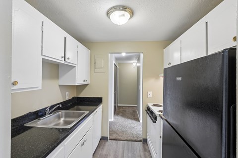 A black fridge in a kitchen with white cabinets.
