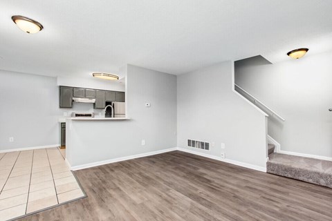 A spacious room with wooden flooring and a staircase.