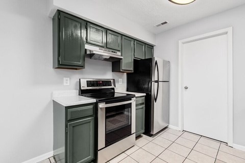 A kitchen with green cabinets and black appliances.