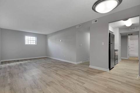 A spacious room with wooden flooring and a refrigerator in the corner.