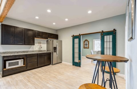 A kitchen with a wooden table and chairs, a refrigerator, and a microwave.