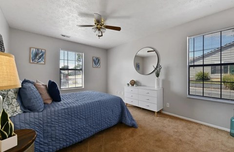 A bedroom with a blue bedspread and a white dresser.