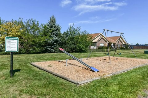 A swing set in a playground with a sign in the background.