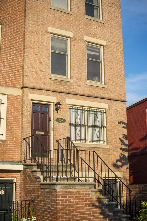 A red brick building with a black iron railing on the stairs.