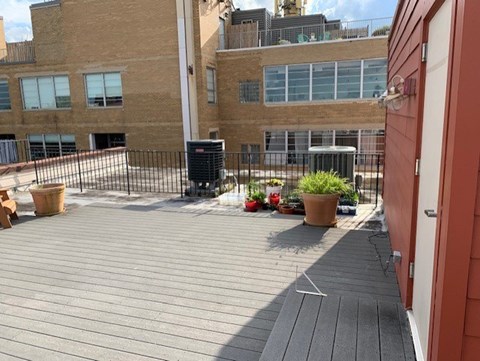 A wooden deck with a black trash can and a red door.