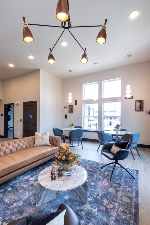 A modern living room with a brown leather sofa, blue chairs, and a coffee table with a vase of flowers on it.