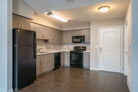 A black refrigerator is in a kitchen with wooden floors and white walls.
