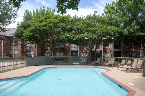 A small pool surrounded by trees and chairs.