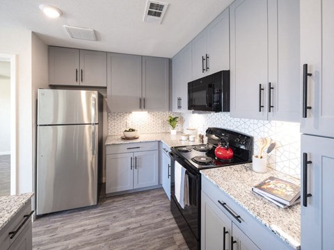 A kitchen with a stainless steel refrigerator and black countertops.