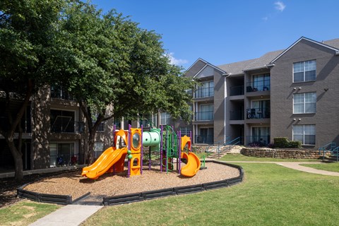 A playground with a slide and a climbing frame in front of apartment buildings.