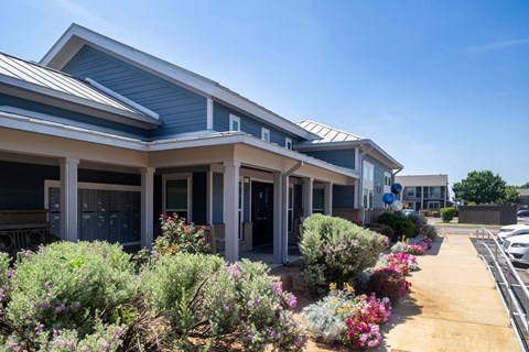 A building with a blue roof and white columns is surrounded by a variety of colorful flowers.
