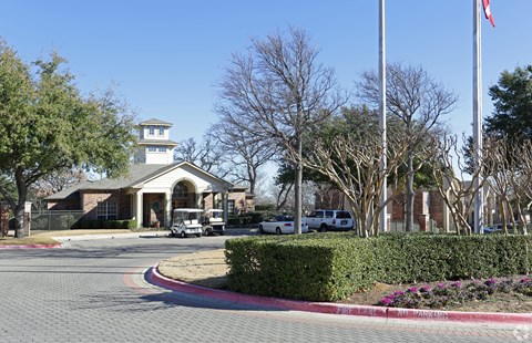 A building with a tower and a flag on top is surrounded by trees and has a driveway leading to it.
