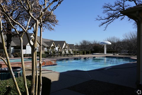 A pool surrounded by trees and a building in the background.