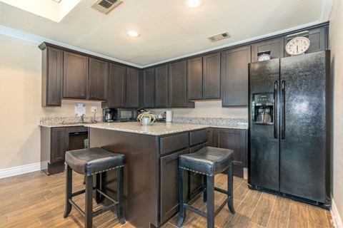 A kitchen with a black refrigerator and bar stools.