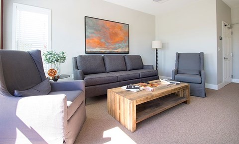 A living room with a grey couch, a wooden coffee table, and a painting on the wall.
