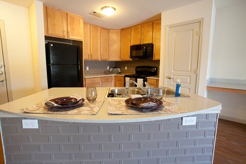 A kitchen with a black fridge and microwave, a white counter top, and wooden cabinets.