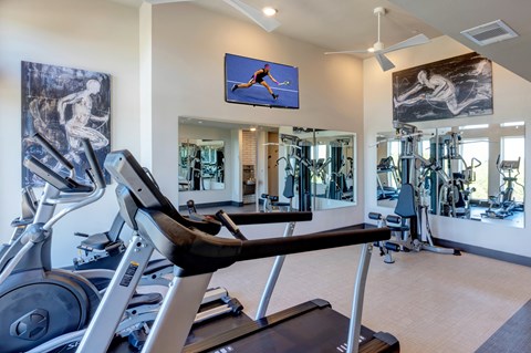 A gym with a row of treadmills and a television mounted on the wall.
