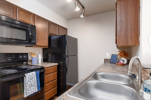 A kitchen with a black refrigerator, black stove, and a black microwave.
