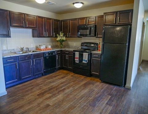 A kitchen with dark wood cabinets and a black fridge.
