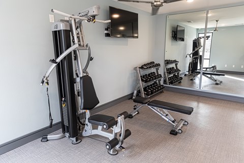 A gym with a weight machine, a bench, and a mirror.