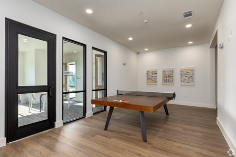 A pool table is in the middle of a room with a black door and a white wall.