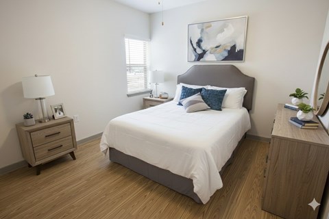 A bedroom with a bed, nightstand, and a painting on the wall.