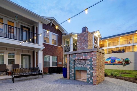 A brick fireplace is in the middle of a patio with a bench and string lights.