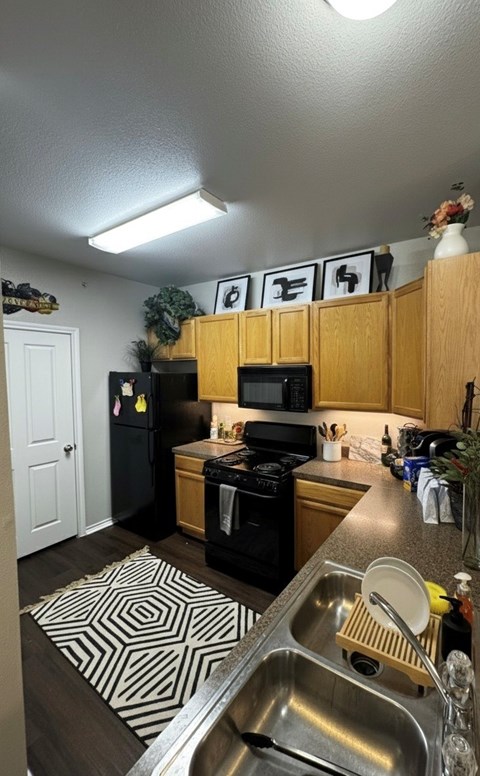 A kitchen with a black fridge and stove, a microwave on the counter, and a sink with a spoon in it.