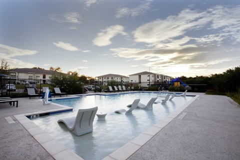 A swimming pool with lounge chairs and a fence in the background.