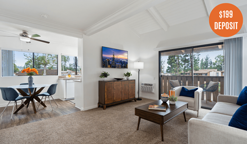 A living room with a dining table and a flat screen TV on the wall.