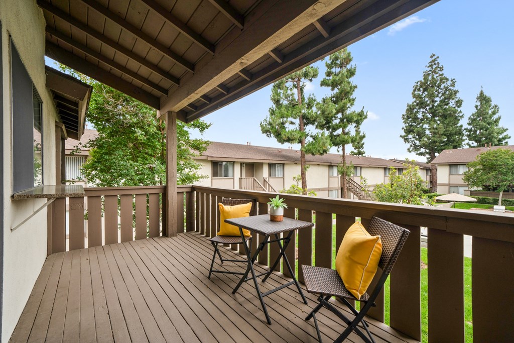 two chairs with yellow pillows sit on a wooden deck with trees in the background