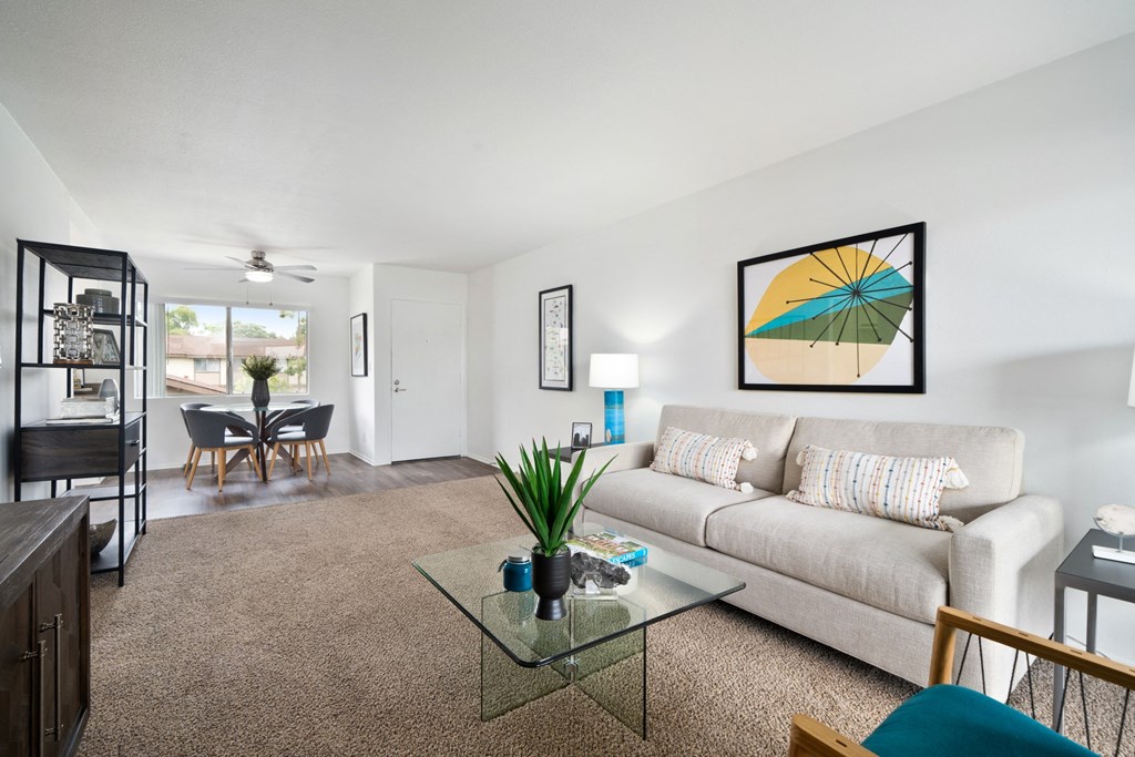a living room with a couch coffee table and a dining room table in the background