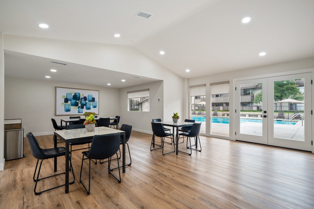 a resident clubhouse with tables and chairs and a pool in the background