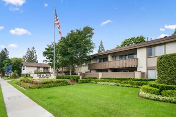 an flag flies in front of a building with a lawn and a sidewalk