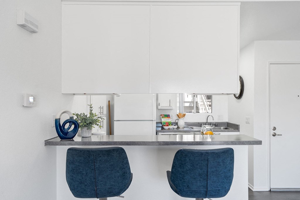 a kitchen with white cabinets and a counter with two blue chairs
