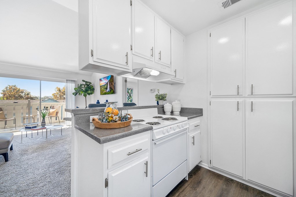 a white kitchen with white cabinetry and a counter top with a basket of fruit